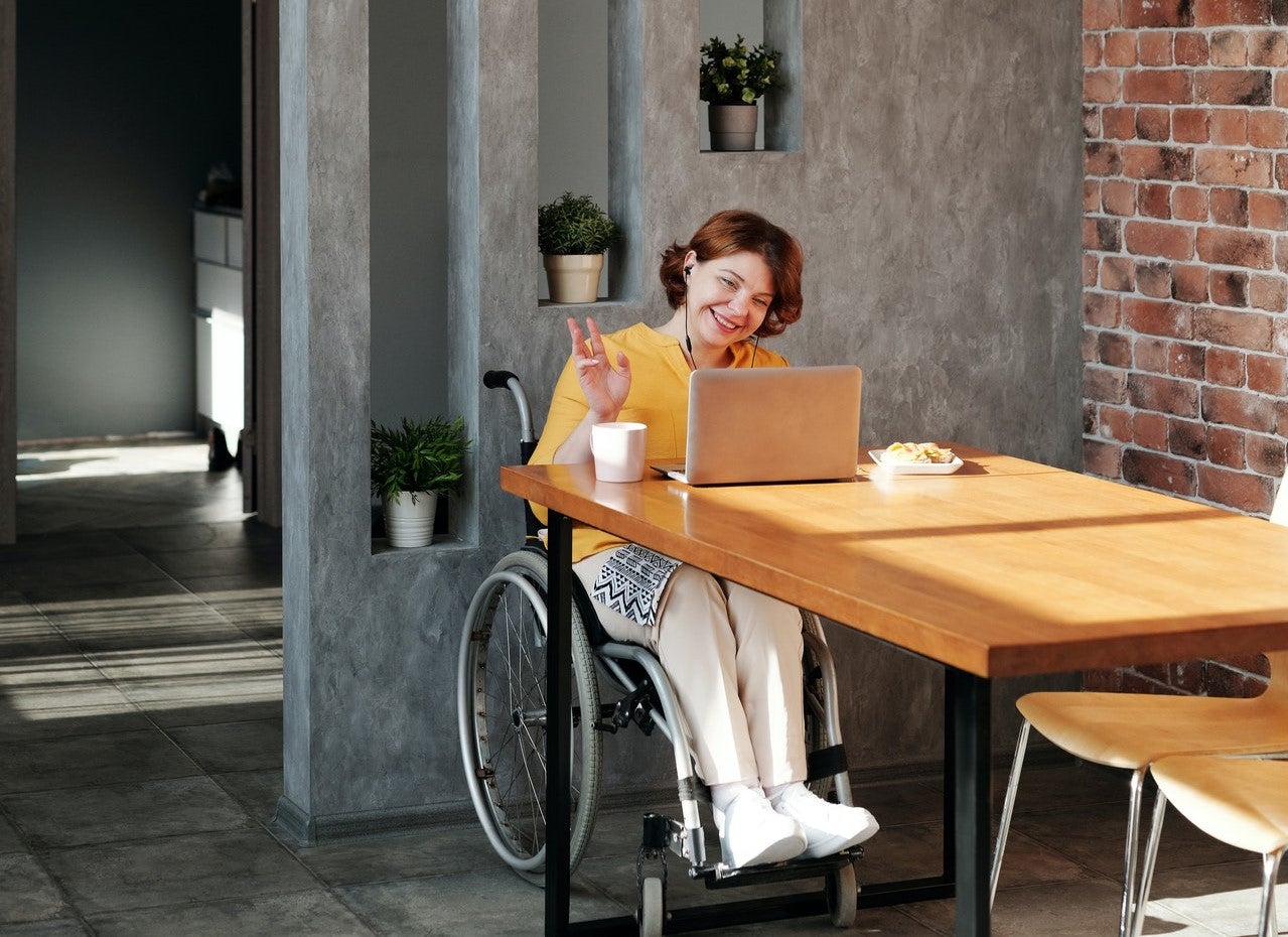 A woman in a wheelchair sits at a cafe table on a computer