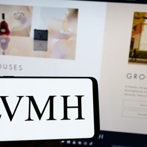 Person holding mobile phone with logo of company LVMH Moet Hennessy Louis Vuitton SE on screen in front of web page. Focus on phone display. Unmodified photo.